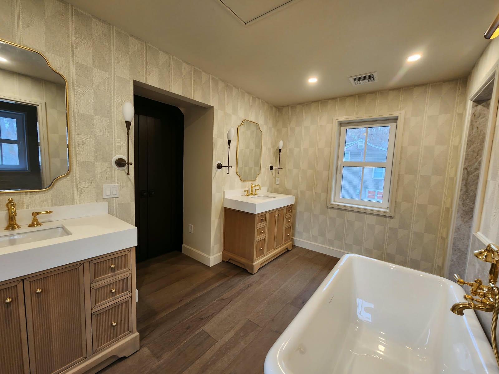Completed bathroom renovation featuring two wooden vanities, wall mirrors, freestanding bathtub, and tiled walls
