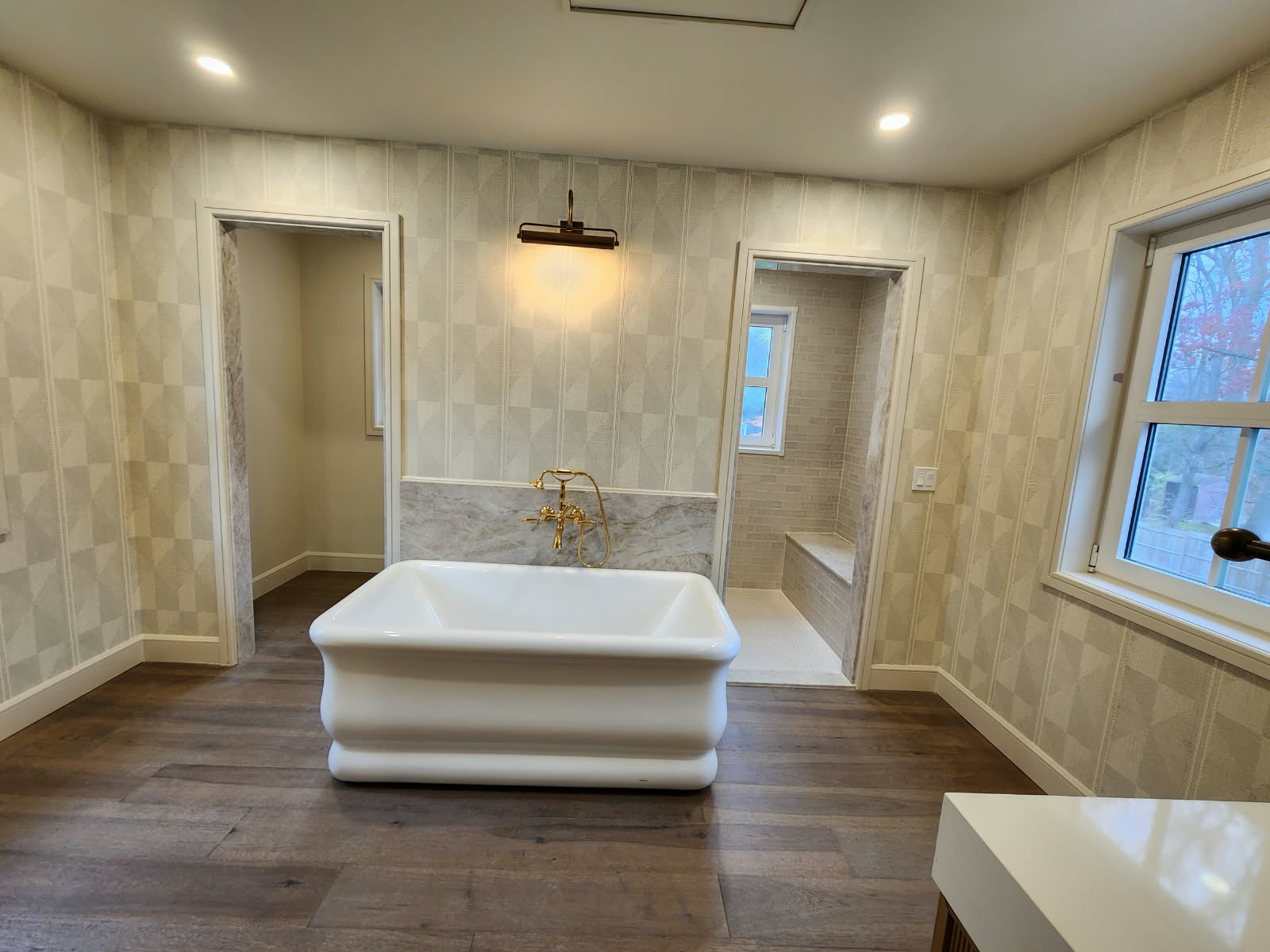 Spacious renovated bathroom featuring a freestanding bathtub, tiled walls, wood-look flooring, and modern lighting