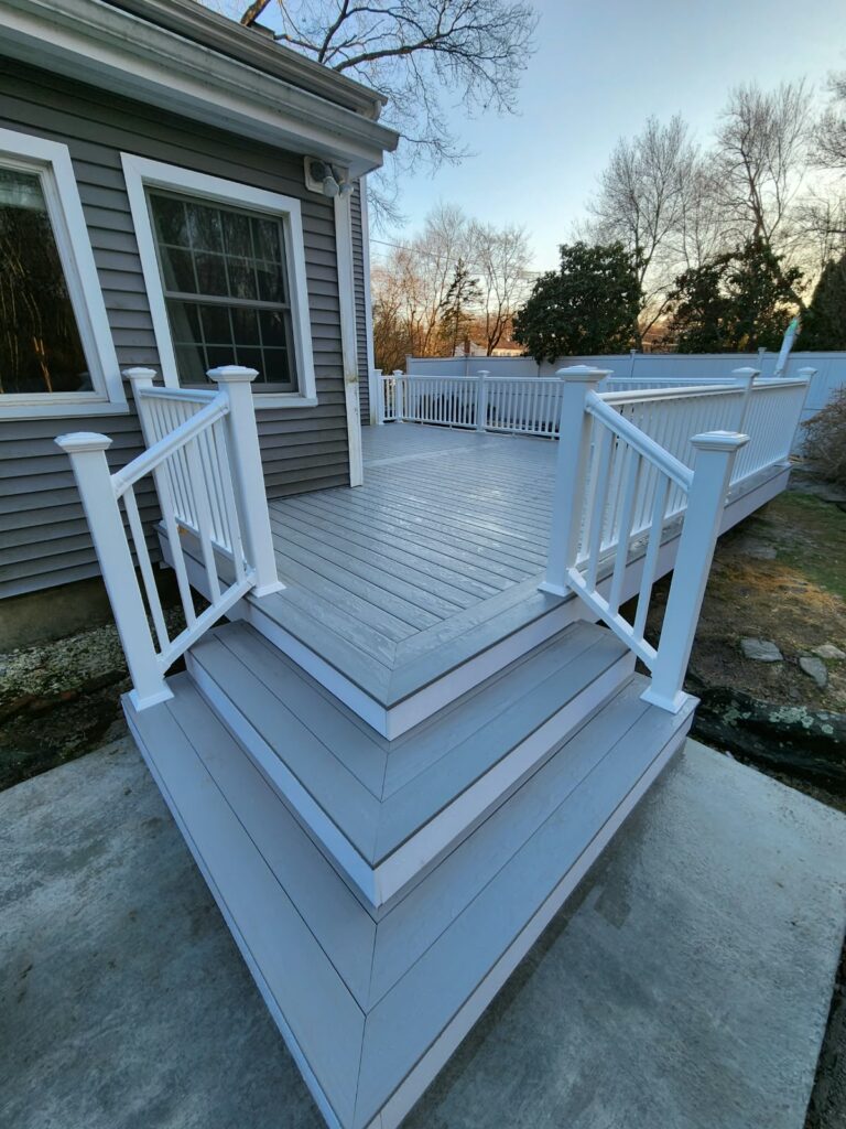 Residential deck with gray decking, white railings, and steps leading to the backyard