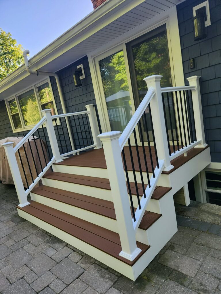 Residential deck stairs with white posts and dark balusters beside a house